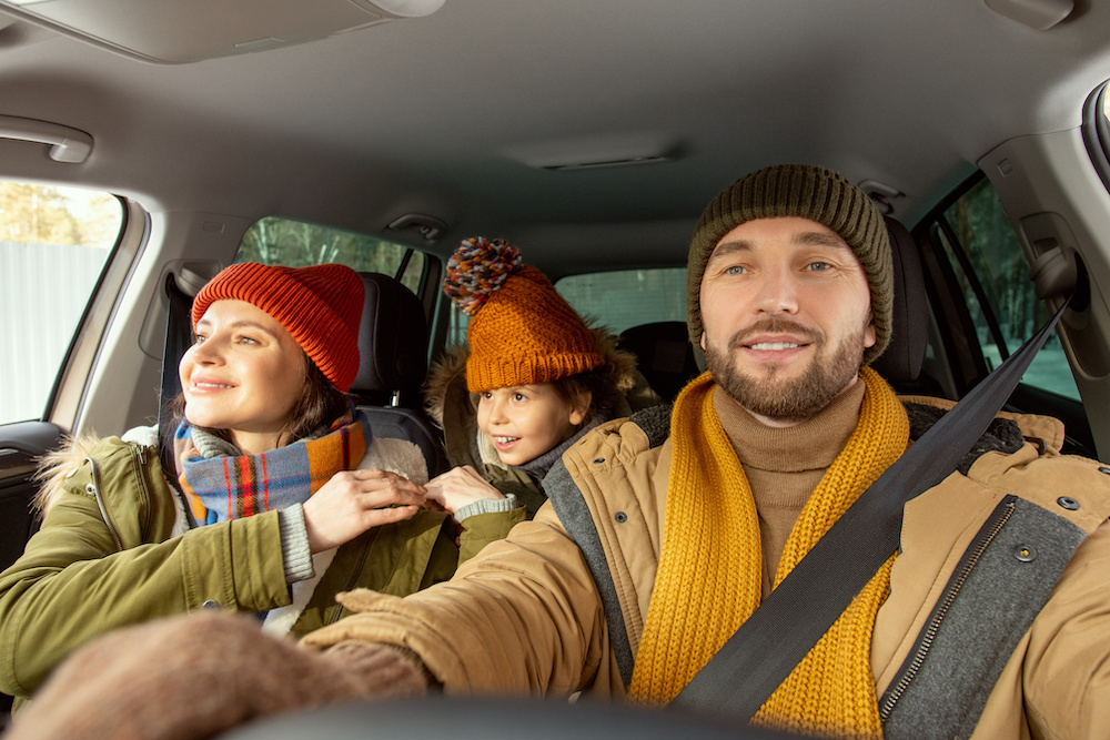 Happy young active man in warm winterwear looking through front window of car